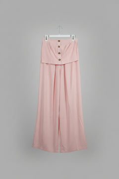 A light pink two-piece set consisting of a button-front top and matching wide-leg pants, hanging in an indoor room.